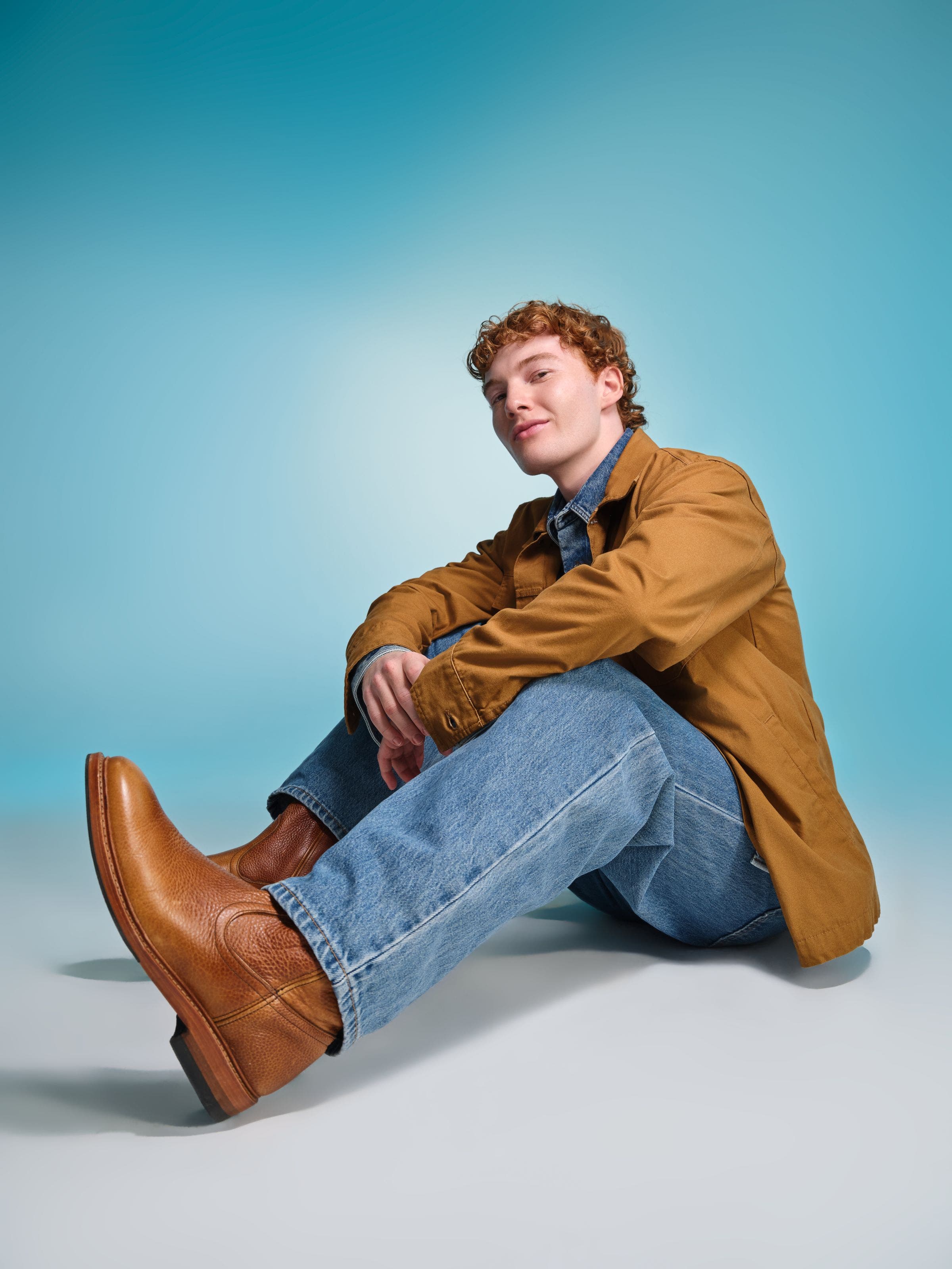 Man wearing a tan jacket, blue jeans, and brown leather boots.