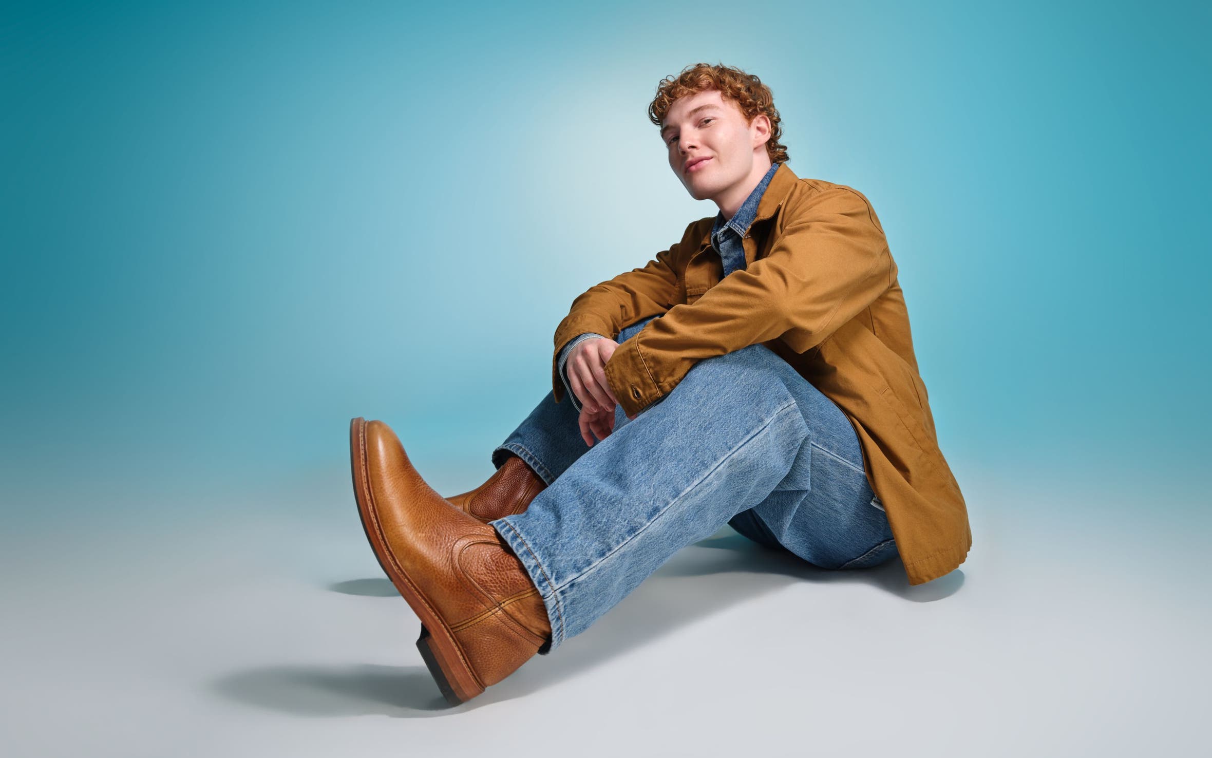 A man wearing brown boots, denim and a brown jacket.