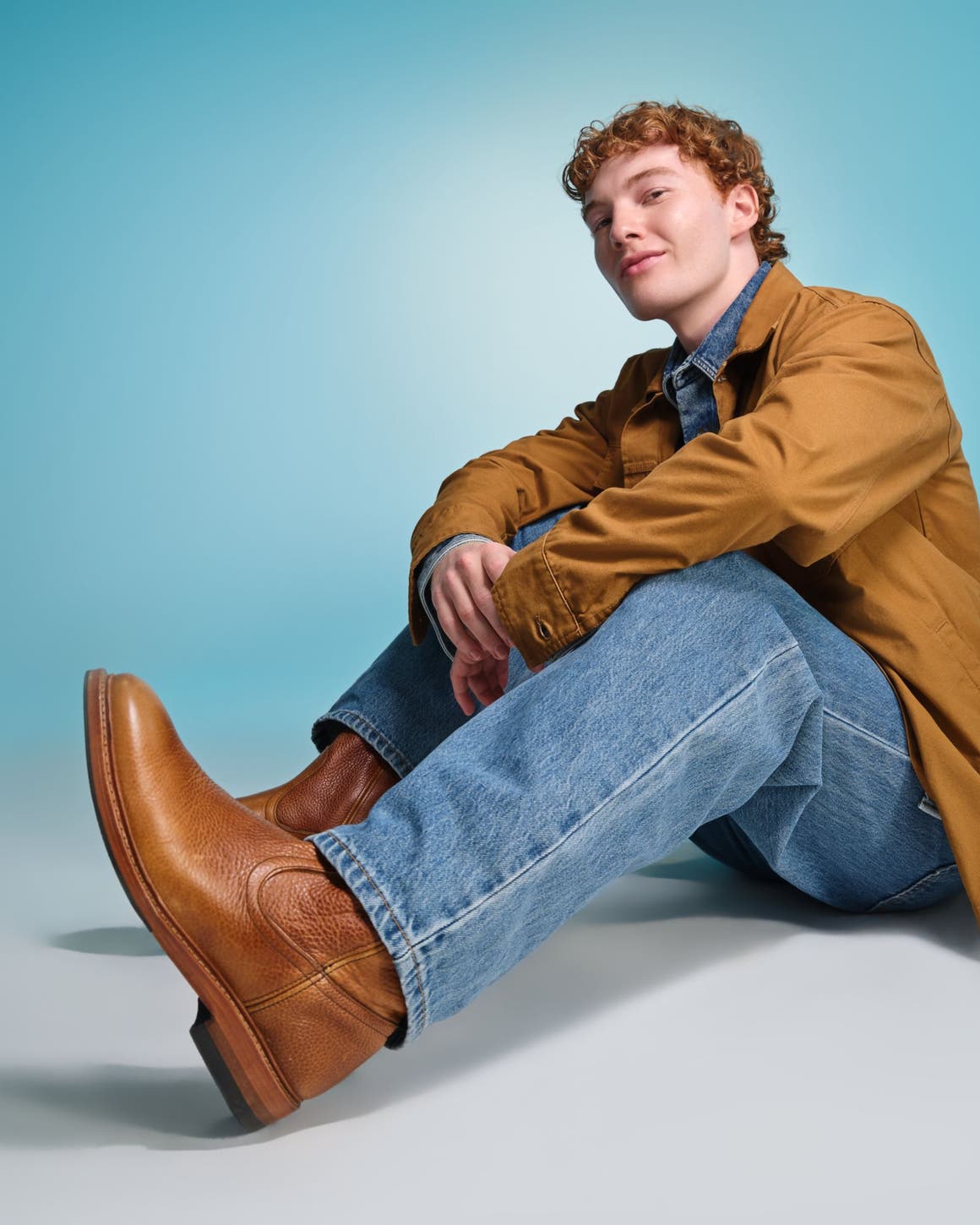 A man wearing brown boots, denim and a brown jacket.