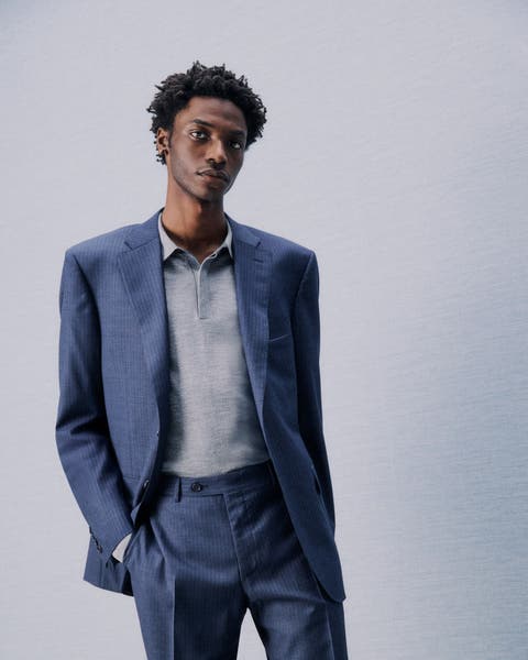 A man wearing a blue suit and grey sweater.