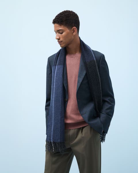 Man wearing a blazer, sweater, trousers and a scarf.