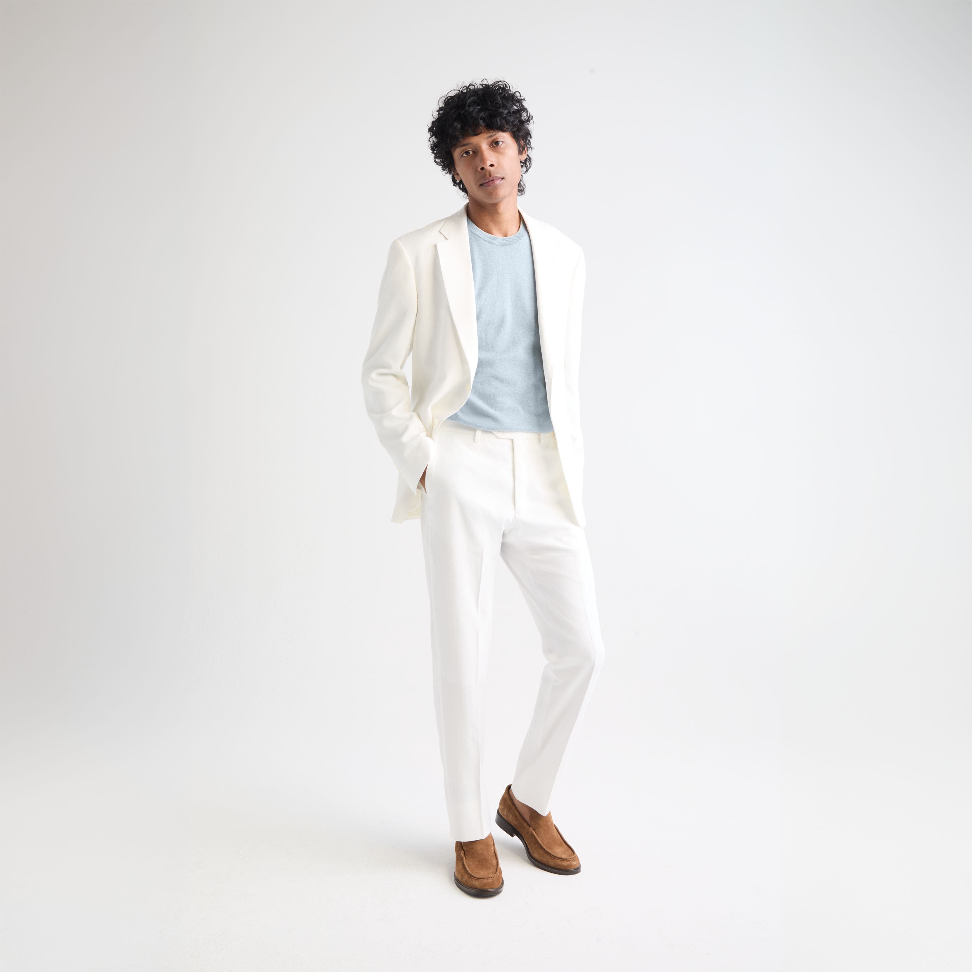 Man wearing a white suit, blue shirt and brown suede loafers.