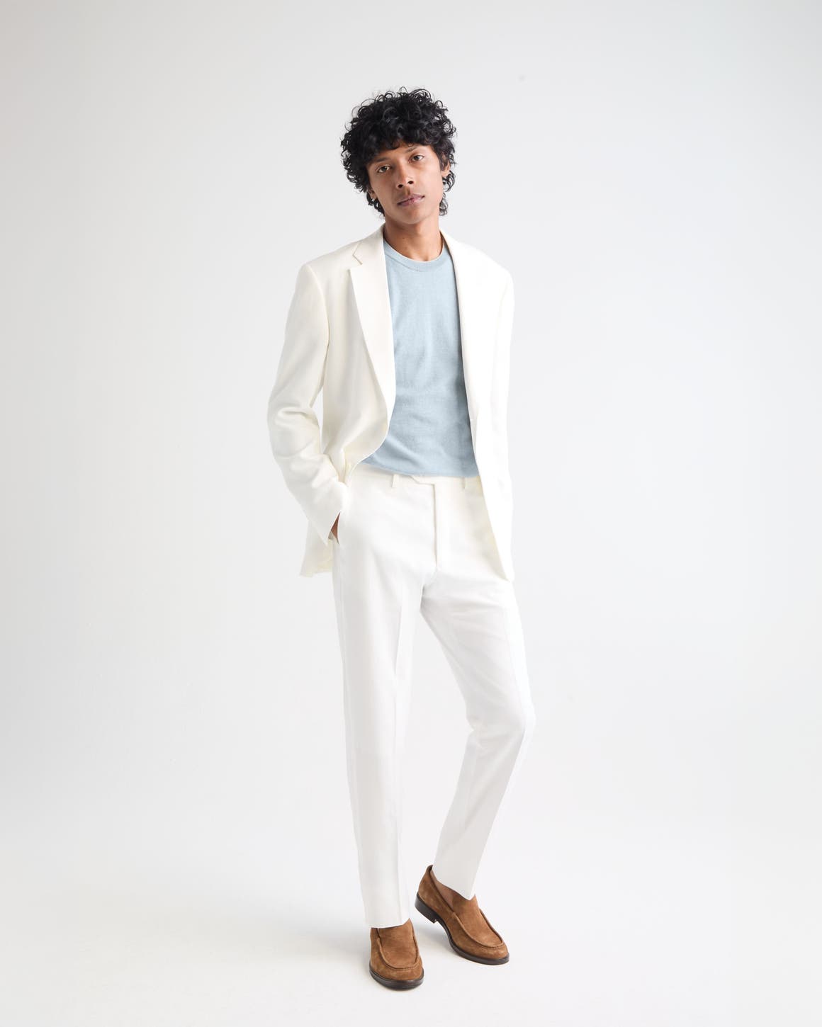 Man wearing a white suit, blue shirt and brown suede loafers.