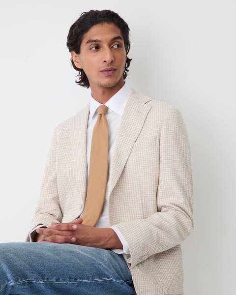 Man in a tan blazer, white button-down, caramel tie and jeans. 