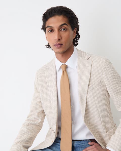 A man in jeans, a white button up and a beige blazer.