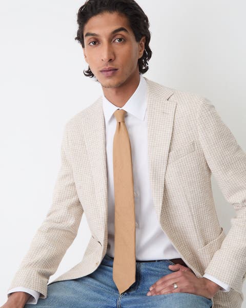 A man in jeans, a white button up and a beige blazer.