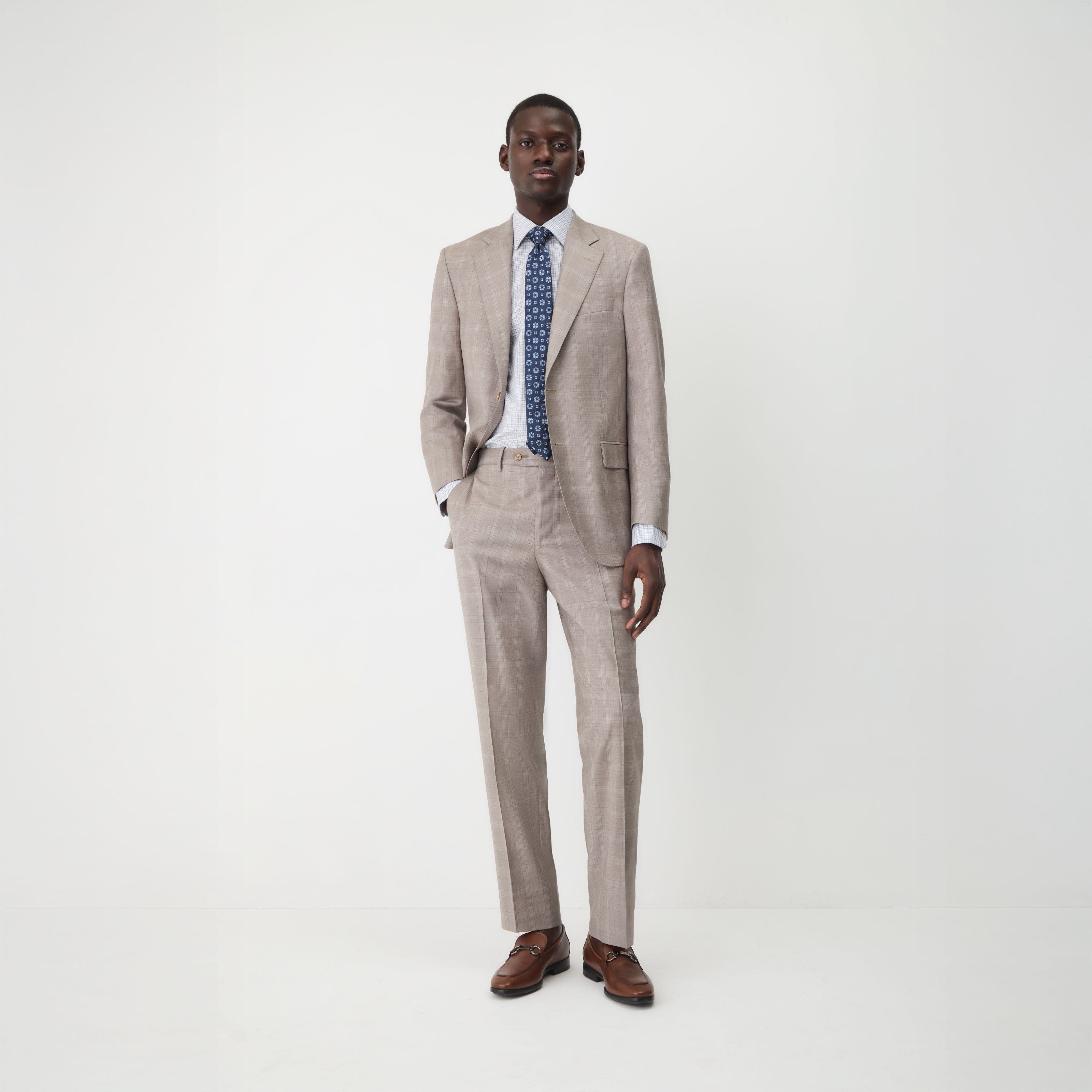 A man wearing a tan suit with a checked shirt and medallion tie.