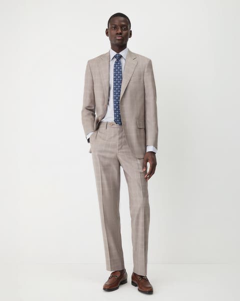 A man wearing a tan suit with a checked shirt and medallion tie.