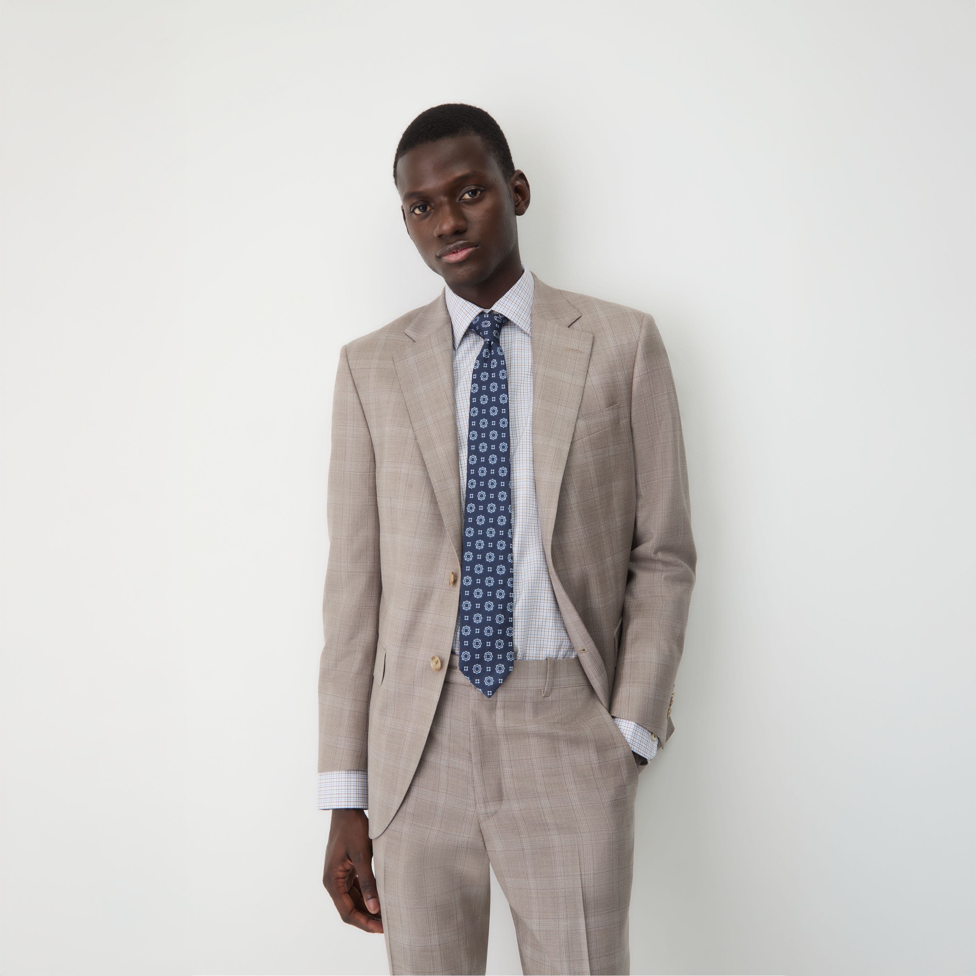 A man wearing a tan suit with a checked shirt and medallion tie.
