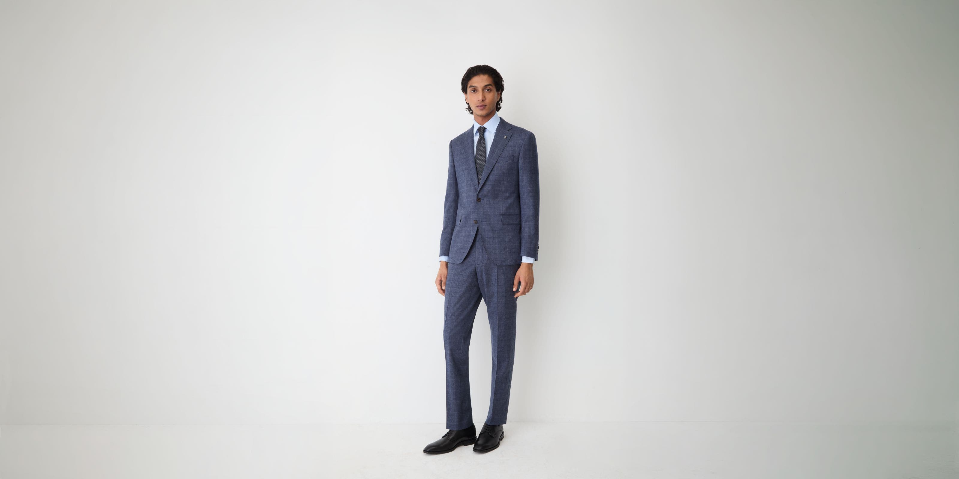 A man wearing a blue suit, dress shirt, tie, and dress shoes.