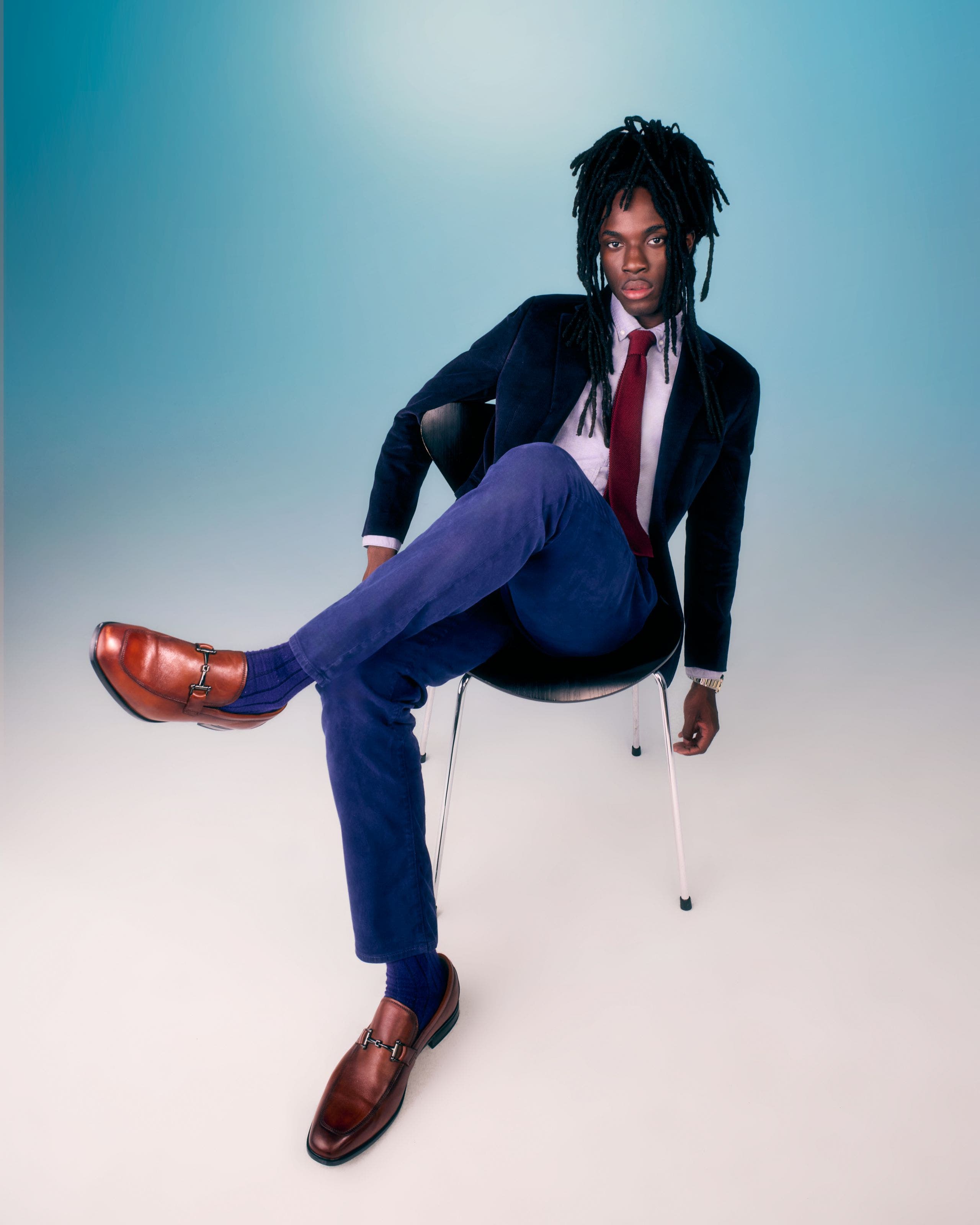 Man wearing a navy suit, a white dress shirt, a red tie and brown shoes.
