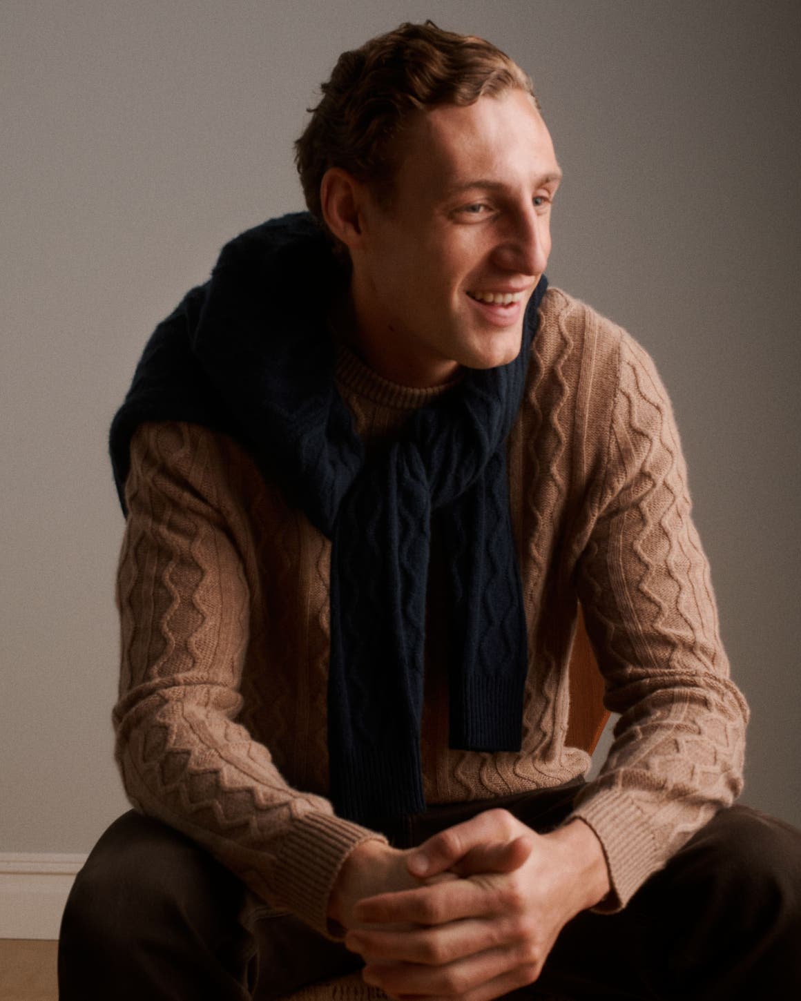 A man wearing a textured camel crewneck sweater, a navy knit layered over his shoulders.