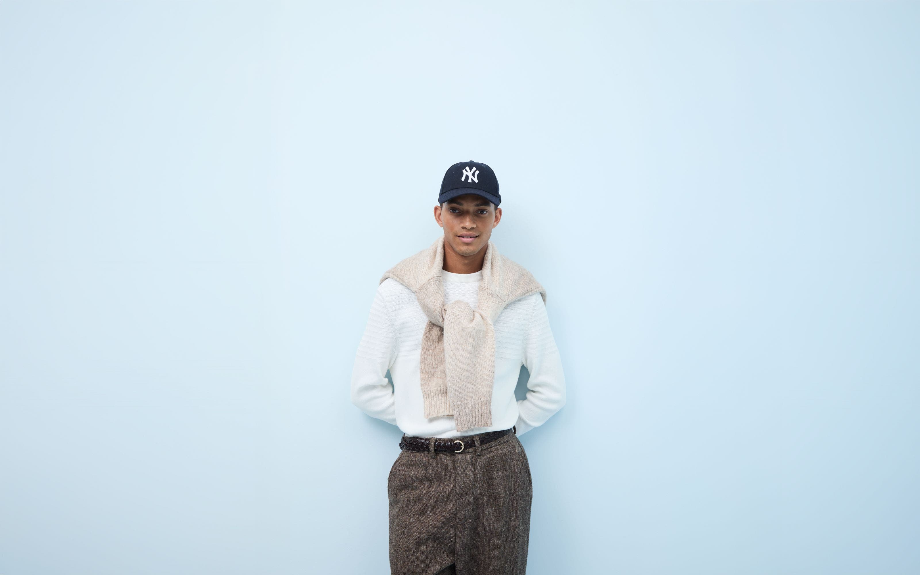 A man wearing two sweaters, tweed pants a Yankees cap.