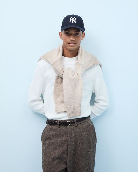 Man wearing a baseball cap, long-sleeve shirt, sweater, wool pants and a belt.