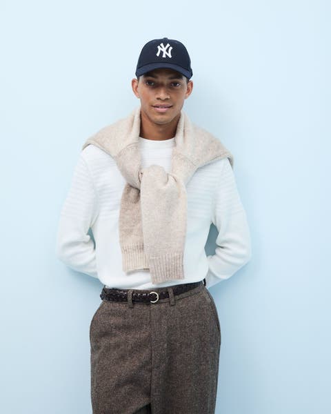 A man wearing two sweaters, tweed pants a Yankees cap.