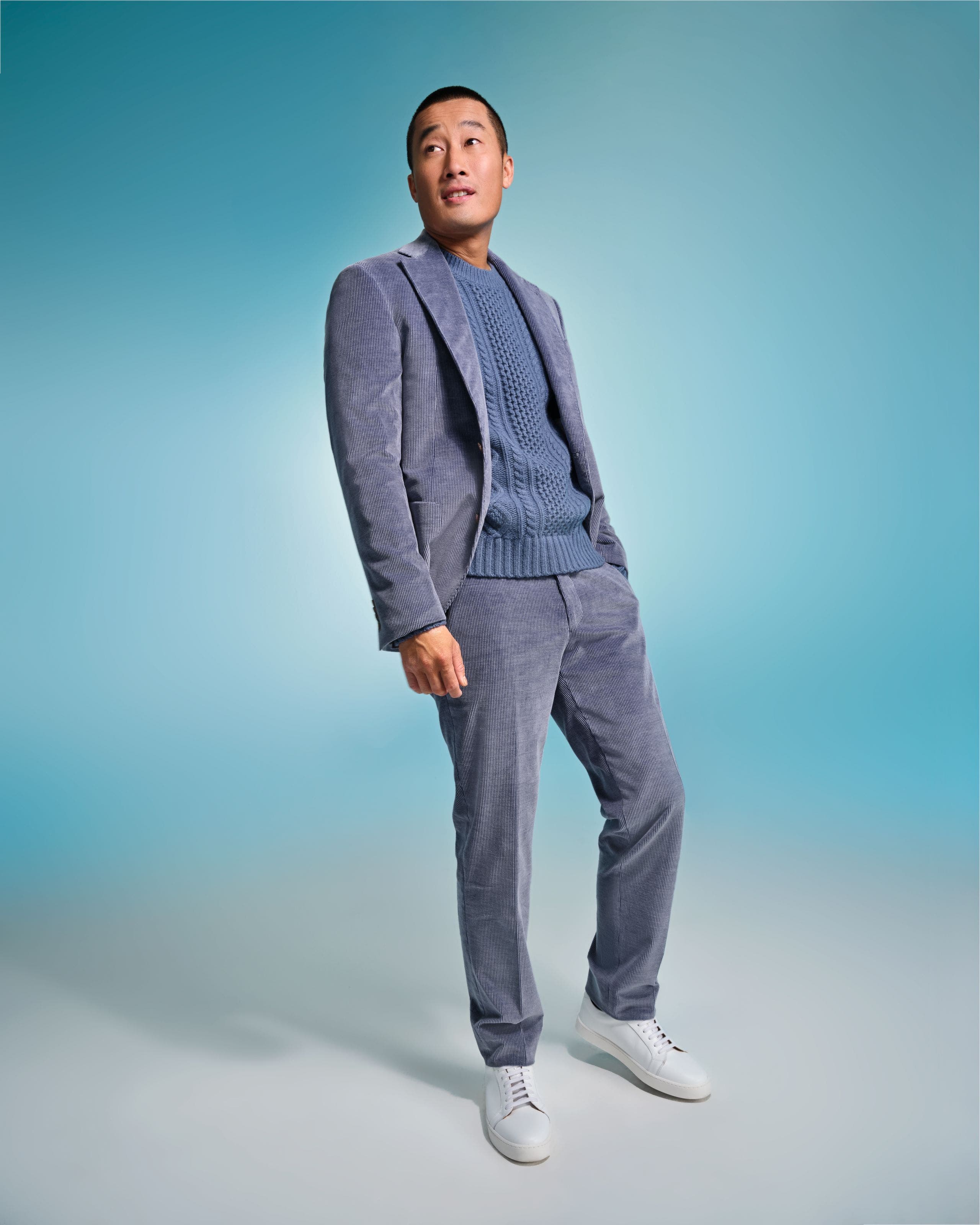 Man wearing a blue-gray textured suit with a matching knit sweater and white sneakers.