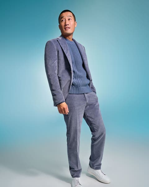 Man wearing a blue-gray textured suit with a matching knit sweater and white sneakers.