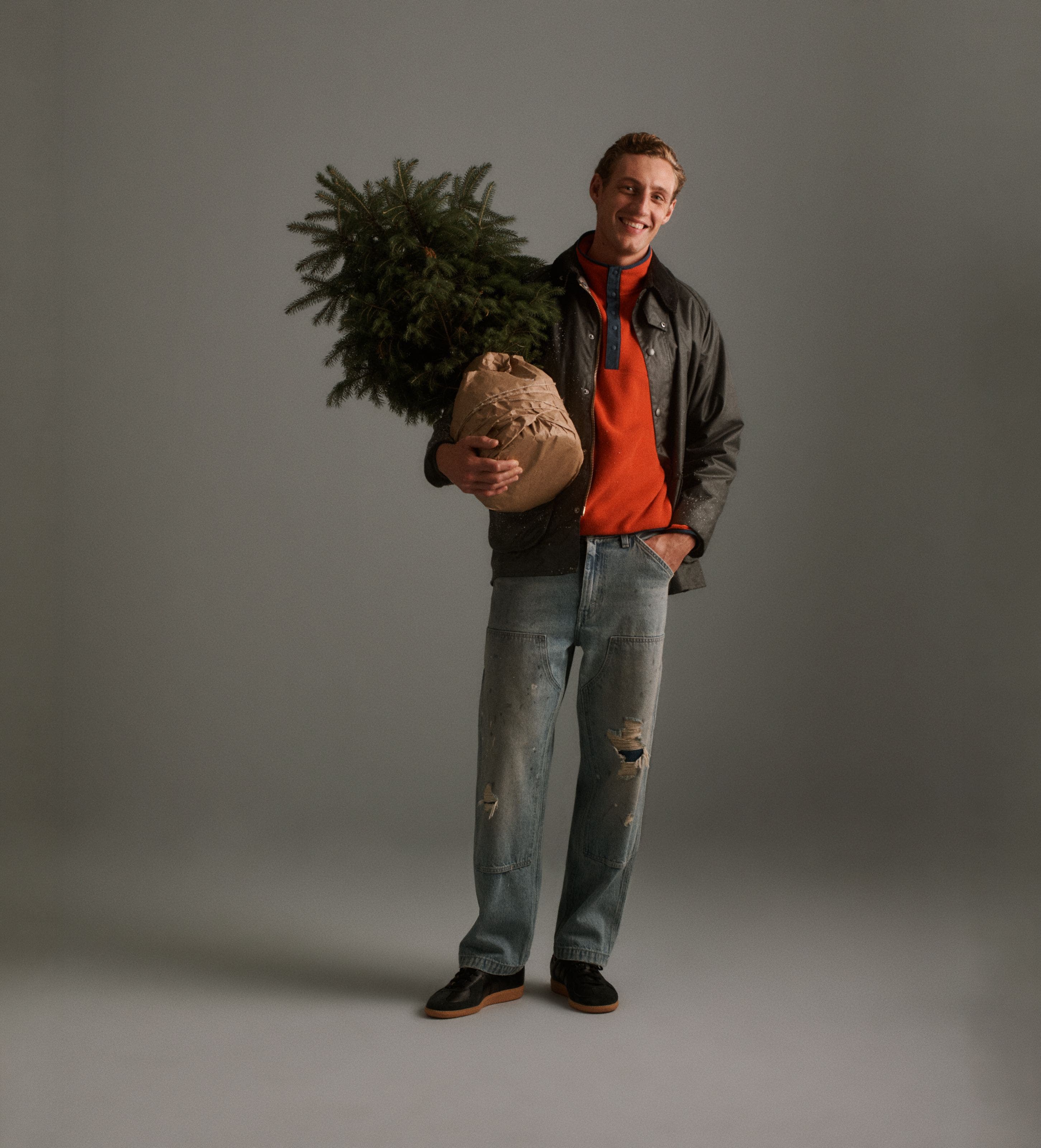 A man wearing a jacket, sweater, and jeans holding a tree.