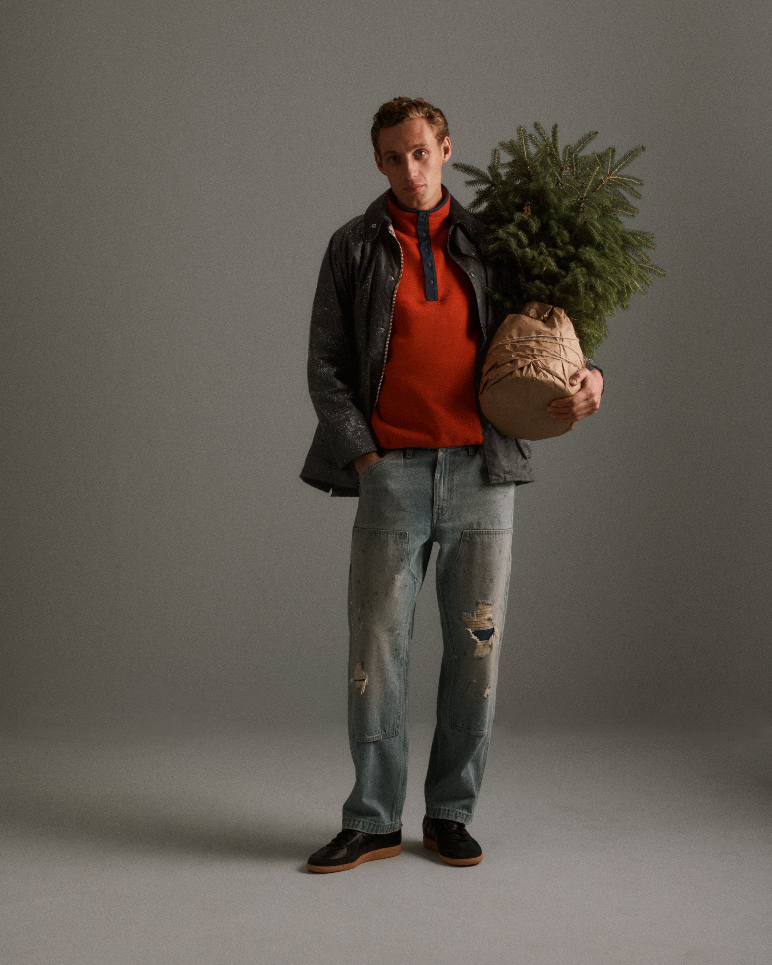A man wearing a red sweater and jeans holding a tree.