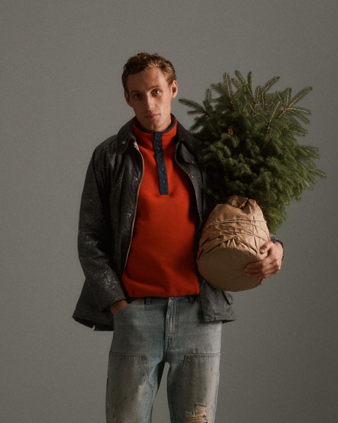 A man wearing a red sweater and jeans holding a tree.