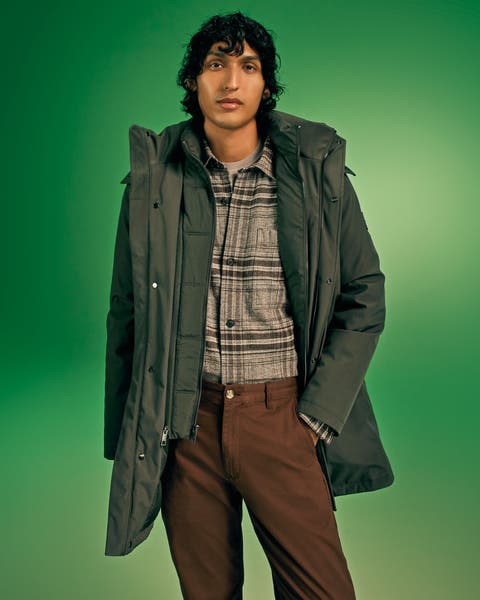 Man in an olive jacket, brown plaid shirt, and brown chinos on green.