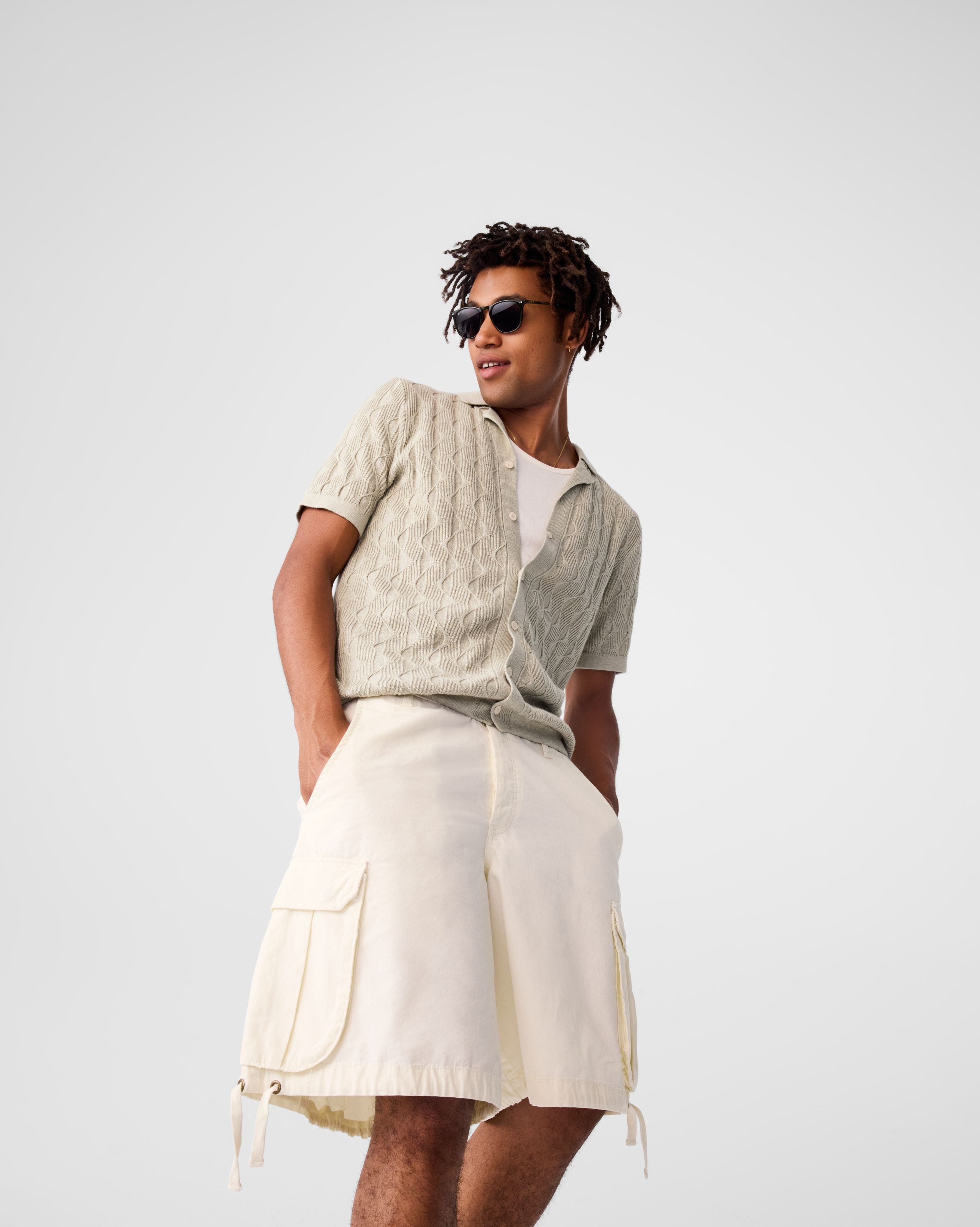 A man wearing a tan cardigan and cream cargo shorts. 