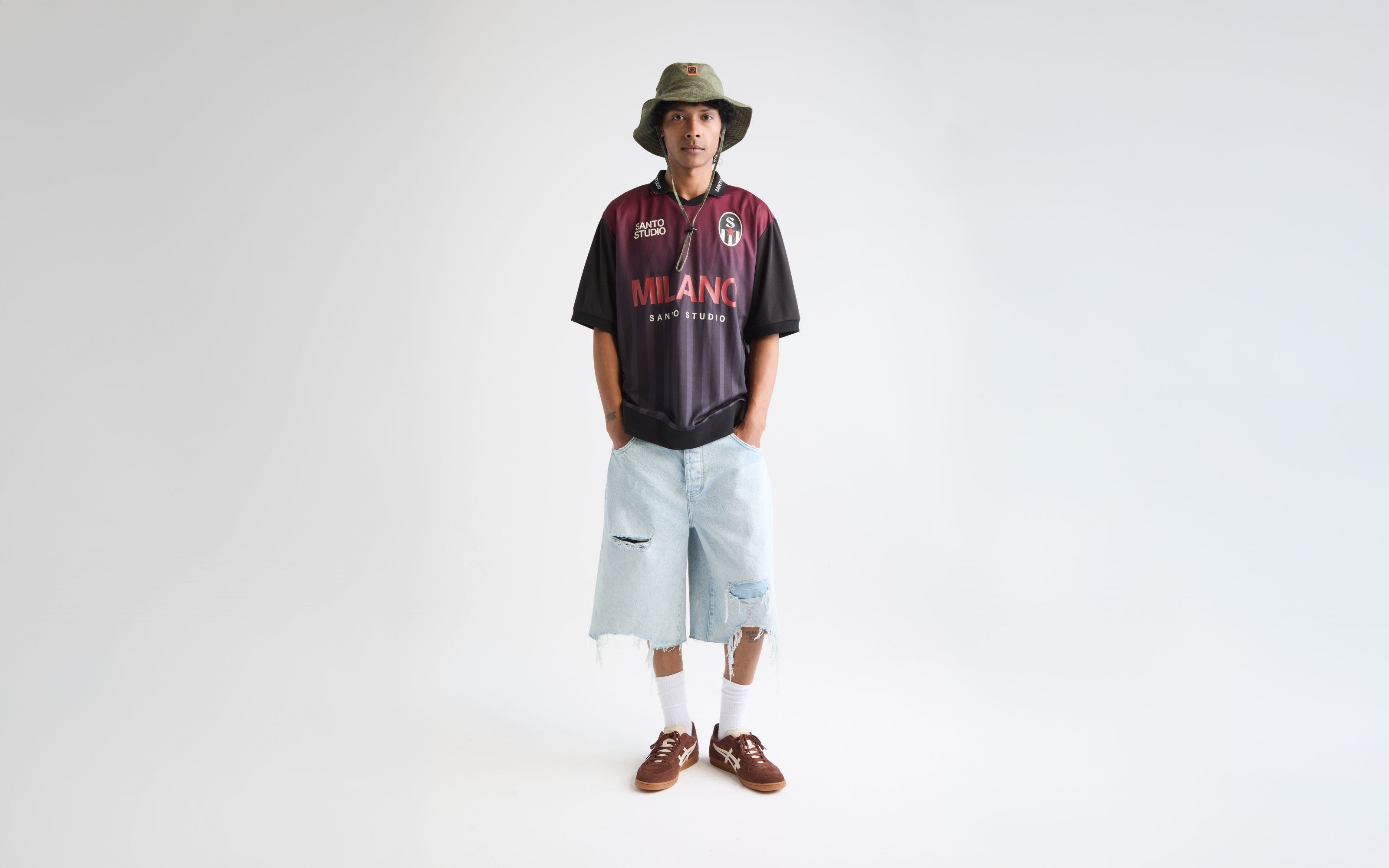 Man wearing a soccer jersey, jean shorts, bucket hat and sneakers.