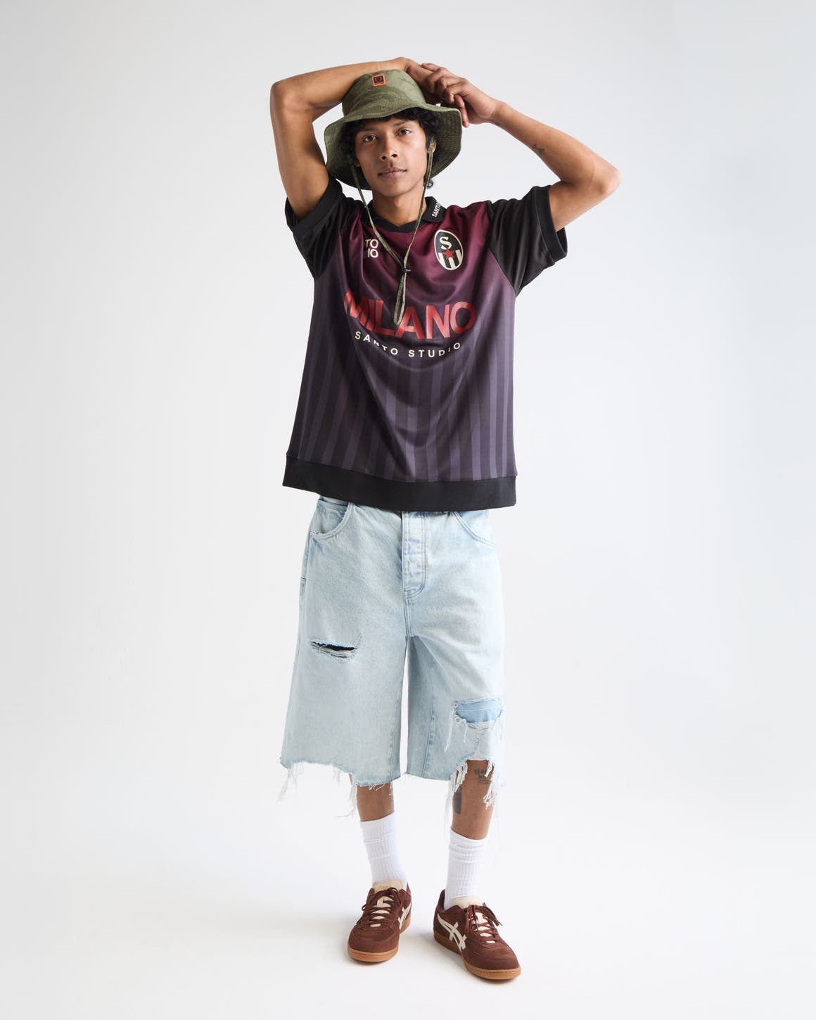 Man wearing a soccer jersey, jean shorts, bucket hat and sneakers.