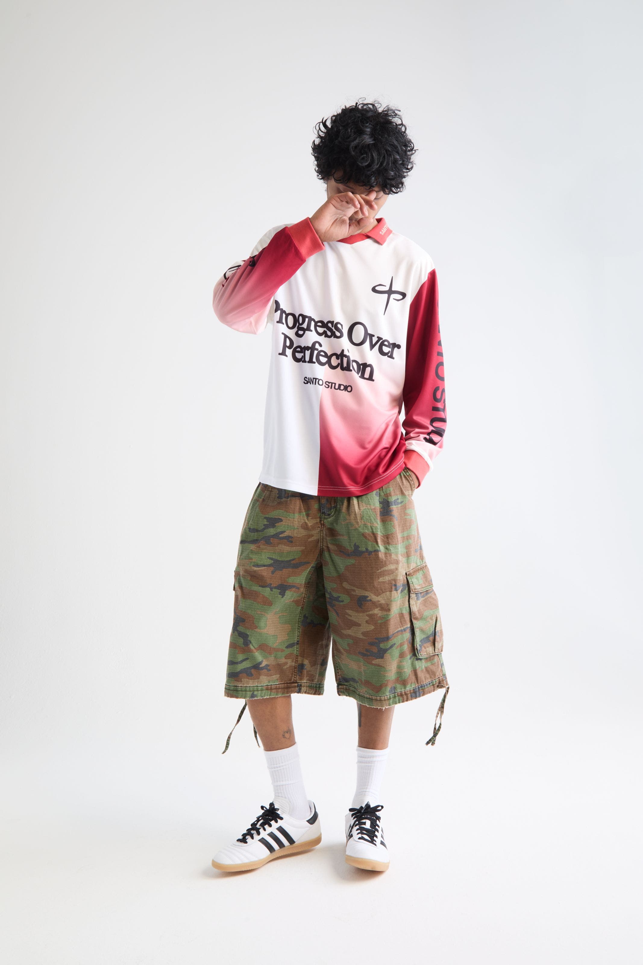 Man wearing a soccer jersey, camo cargo shorts and adidas sambas.