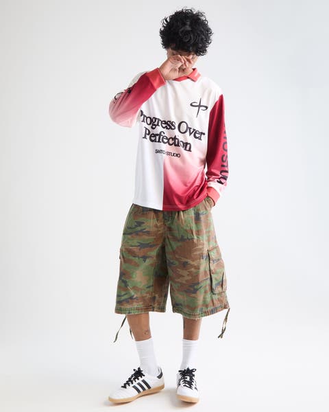 Man wearing a soccer jersey, camo cargo shorts and adidas sambas.