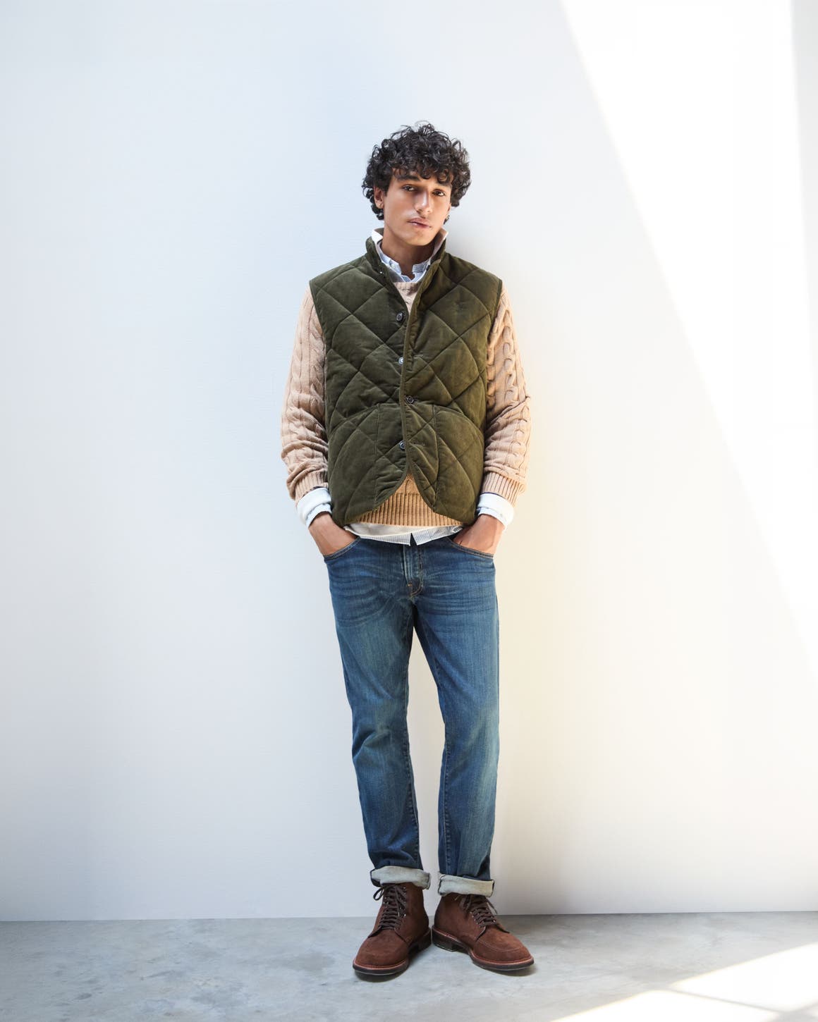 A man wearing vest, shirts, sweater and jeans. 