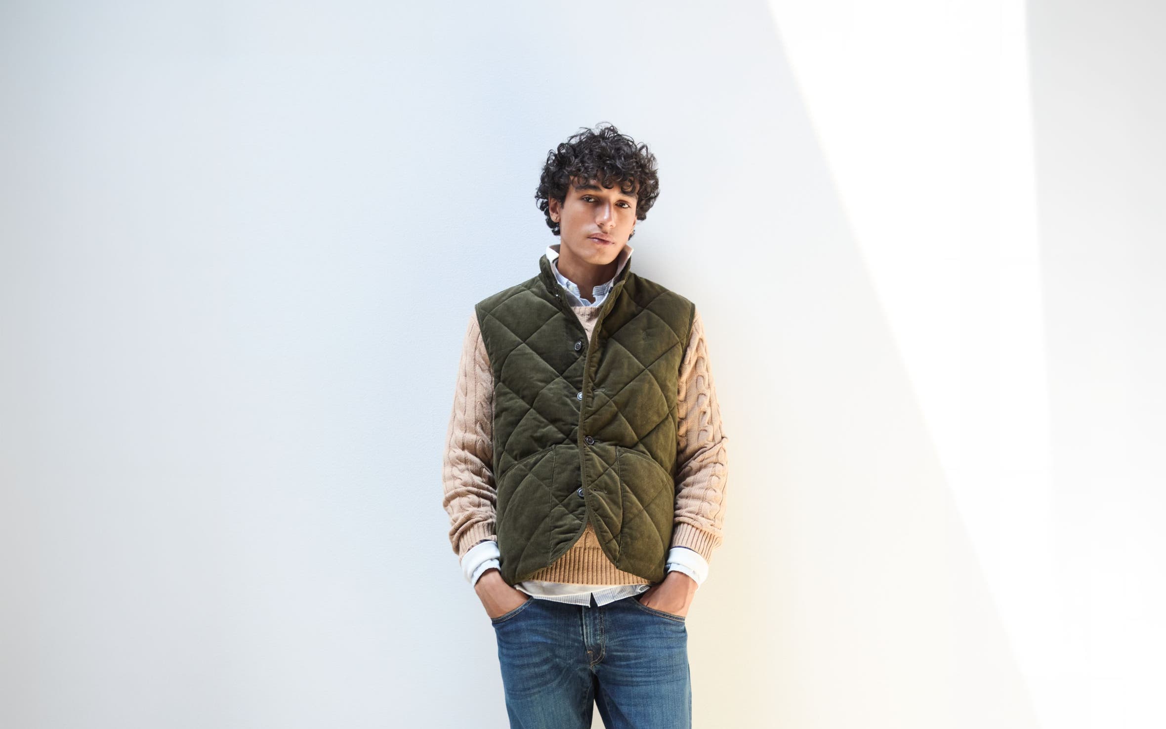 A man wearing vest, shirts, sweater and jeans. 