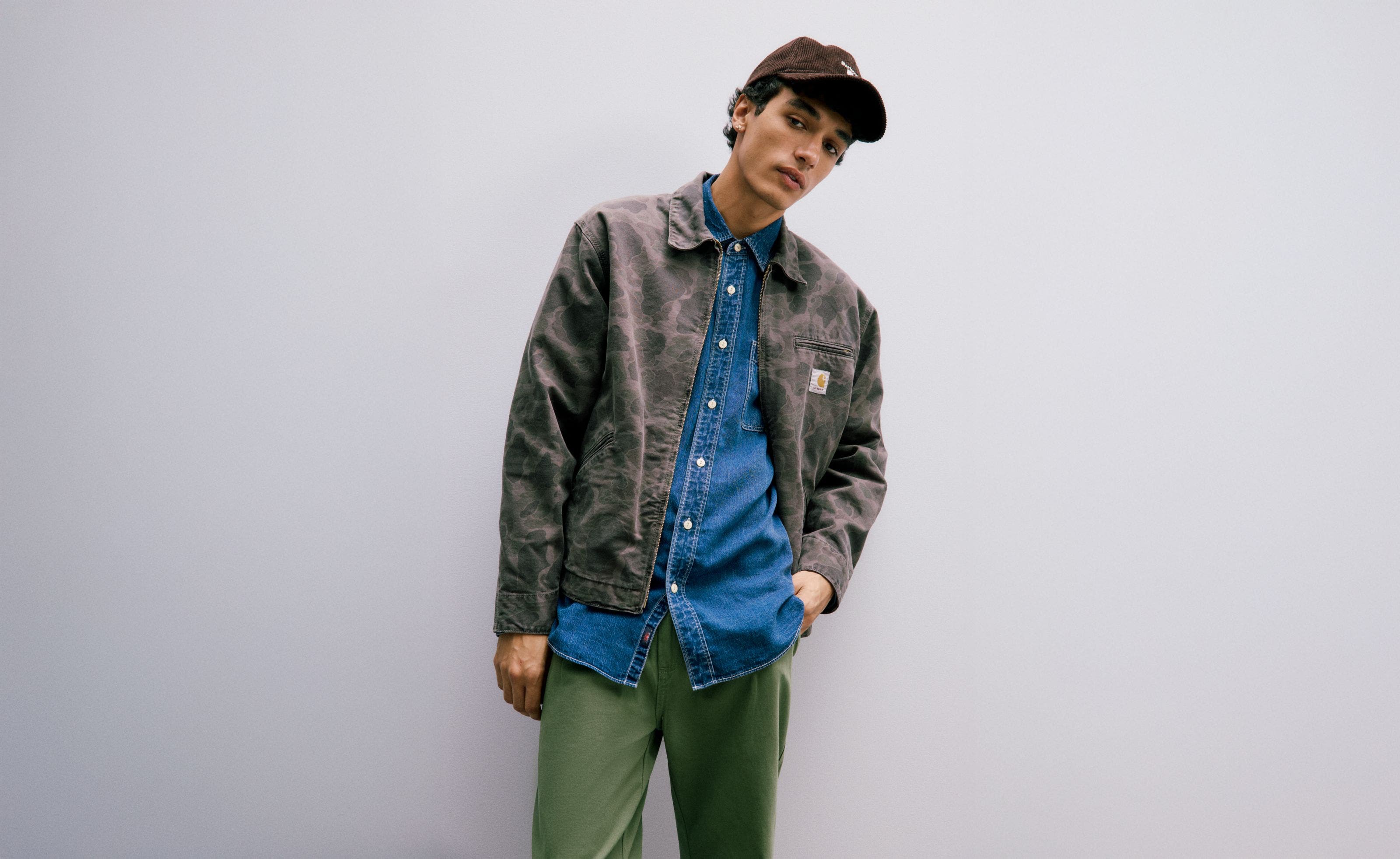 Man wearing a camo jacket, denim shirt and army green pants.