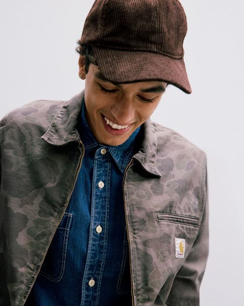 Man wearing a camo jacket, denim shirt and corduroy baseball cap.