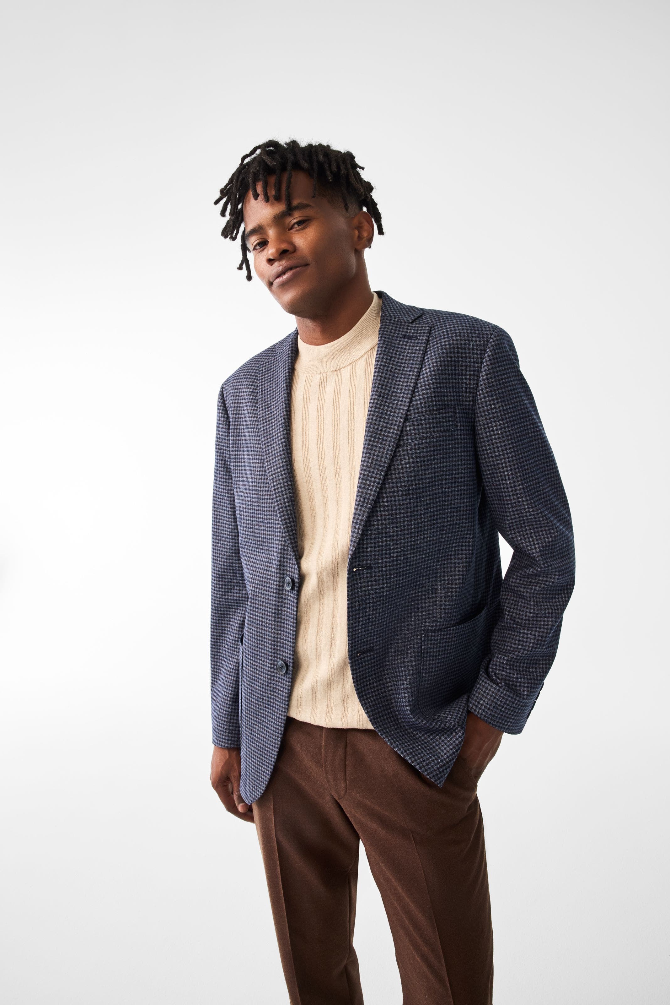 A man wearing a houndstooth blazer with a mock-neck sweater and brown pants.