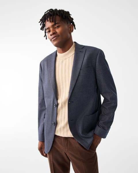 A man wearing a houndstooth blazer with a mock-neck sweater and brown pants.