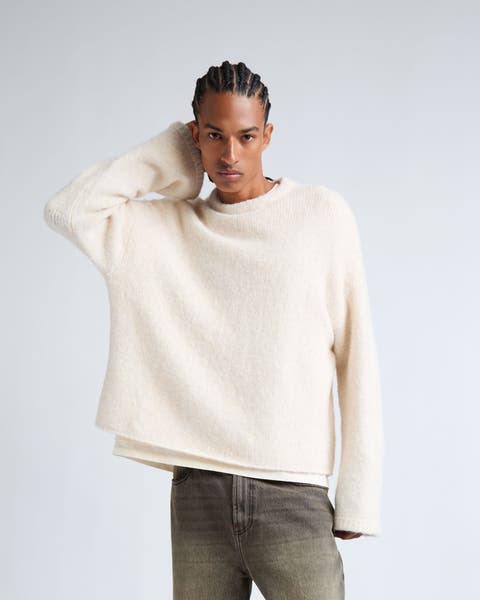 A man wearing a sweater, jeans and sneakers.