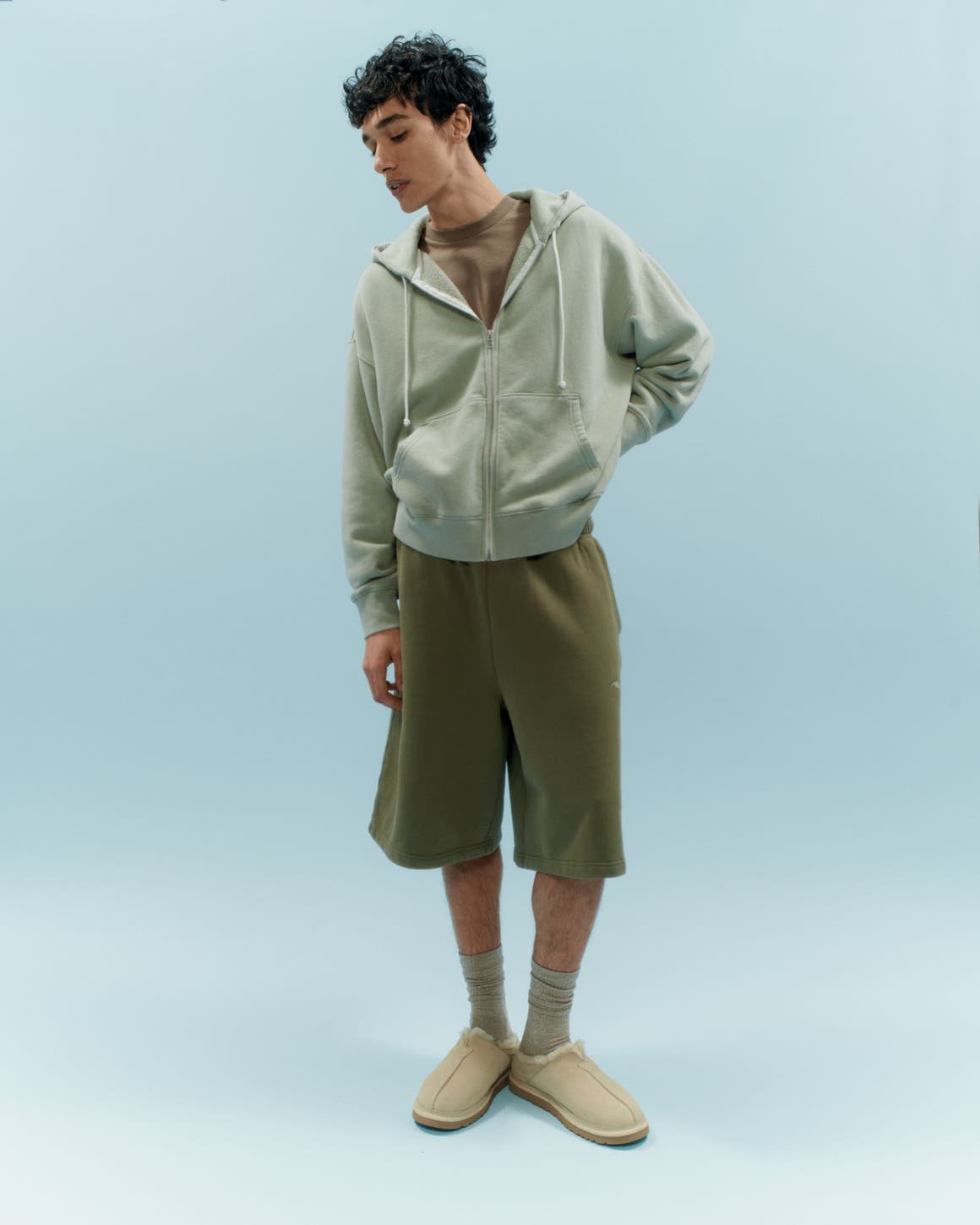 A man wearing an Elwood zip hoodie with sweat shorts, a T-shirt, crew socks and UGG slippers.