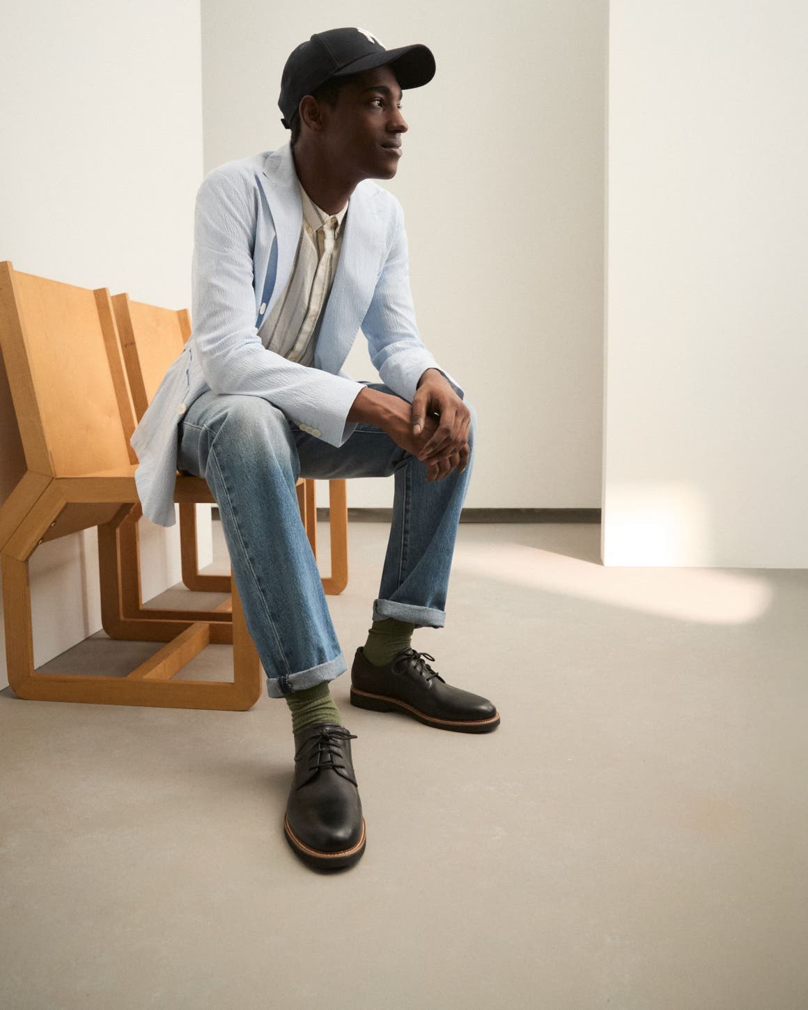 A man wearing a lightweight sport coat, button-down shirt, jeans and ball cap.