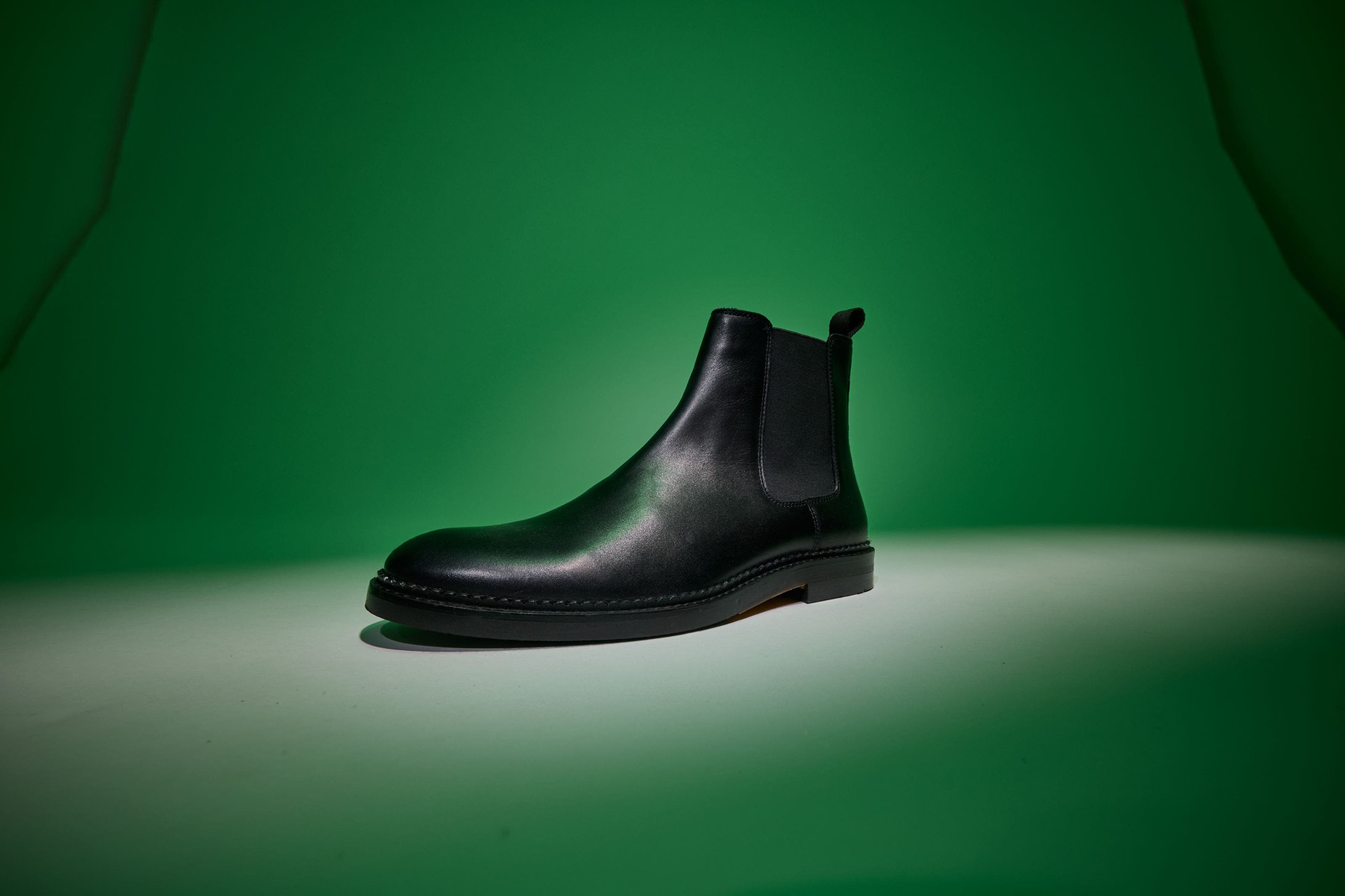 Black leather Chelsea boot on a green background.