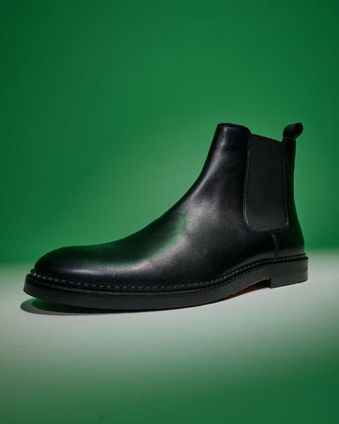 Black leather Chelsea boot on a green background.