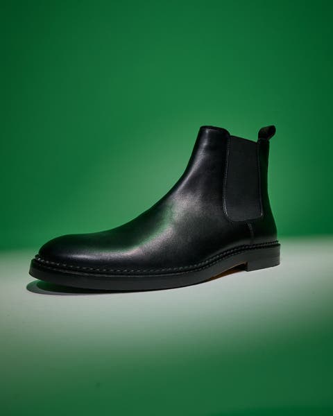 Black leather Chelsea boot on a green background.