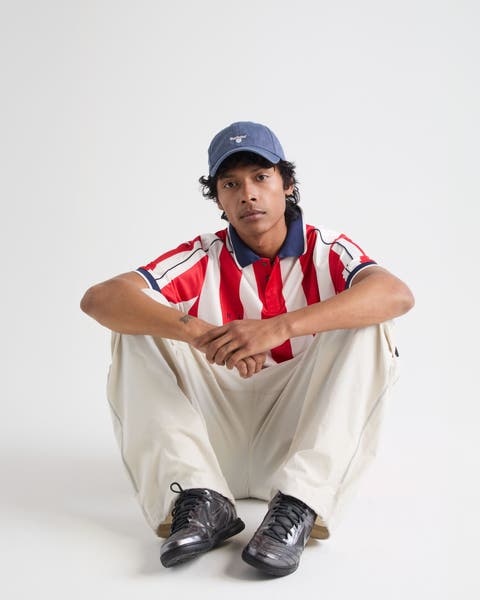 Man wearing a cap, striped jersey, pants and sneakers.