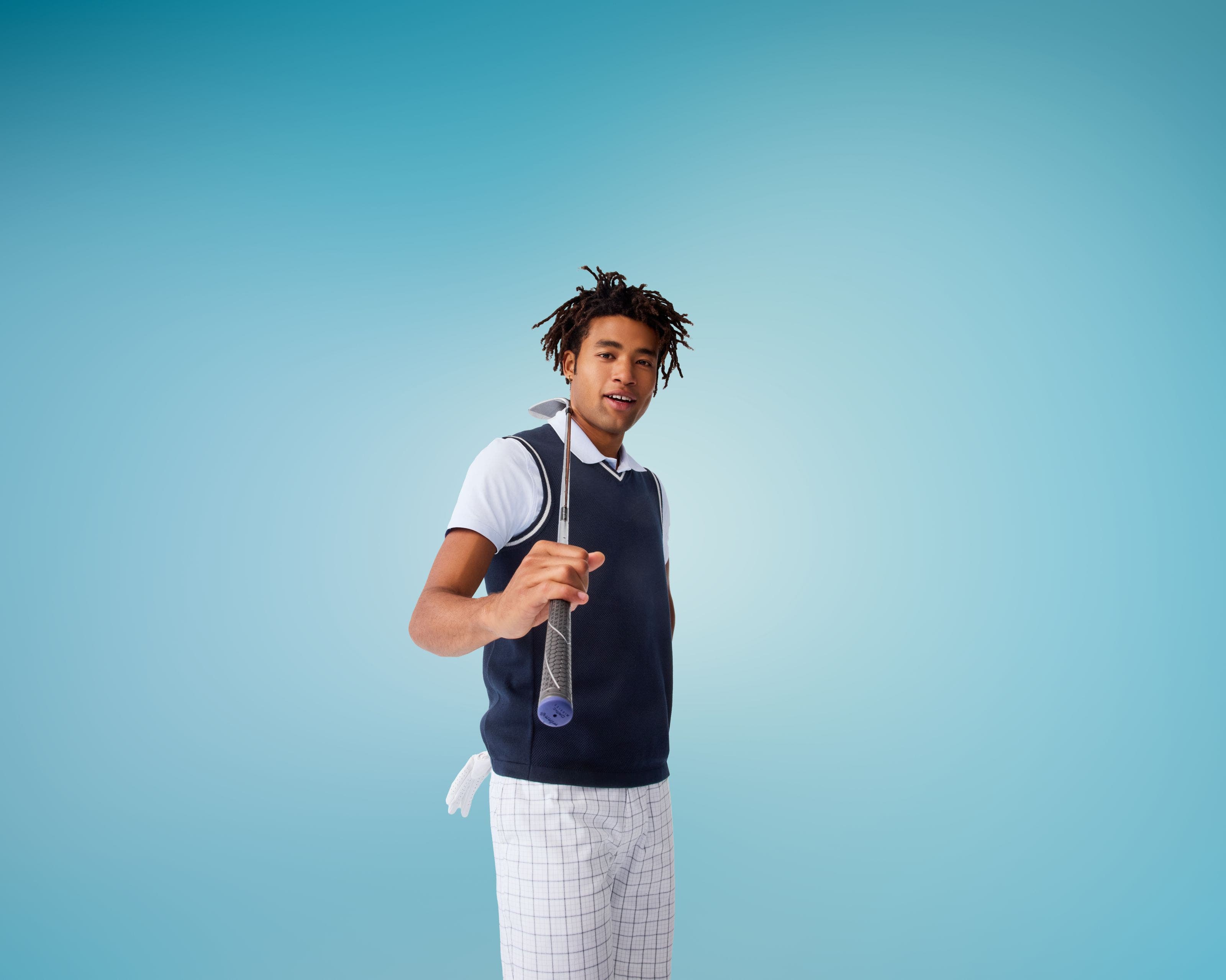 A man wearing a navy sweater vest, a polo shirt and white checked bottoms.