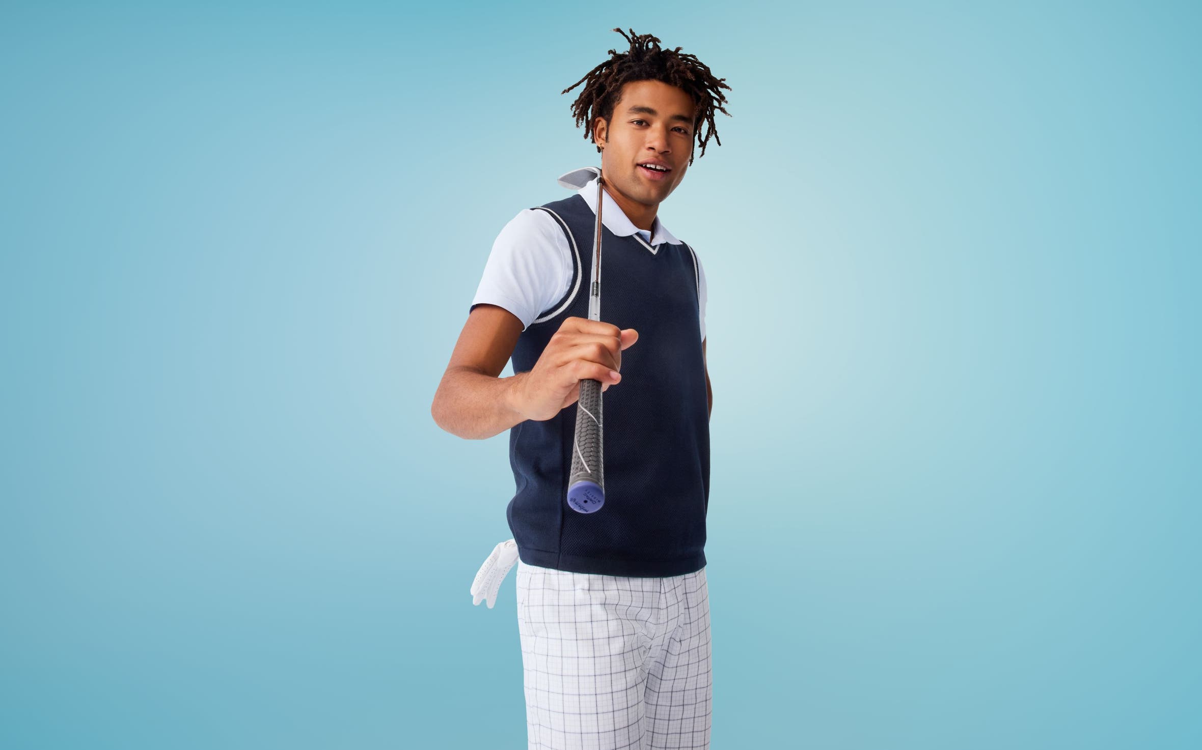 A man wearing a navy sweater vest, a polo shirt and white checked bottoms.