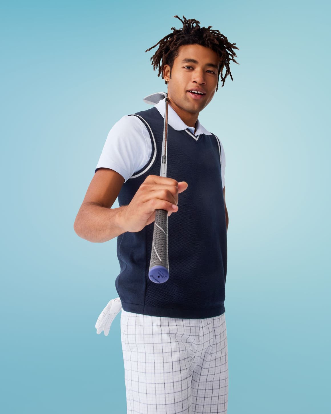 A man wearing a navy sweater vest, a polo shirt and white checked bottoms.