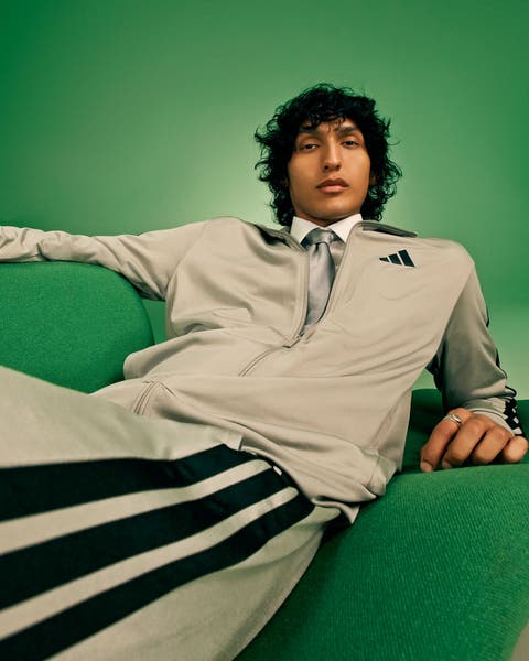 Man in a gray track jacket and three-stripe pants with a tie.