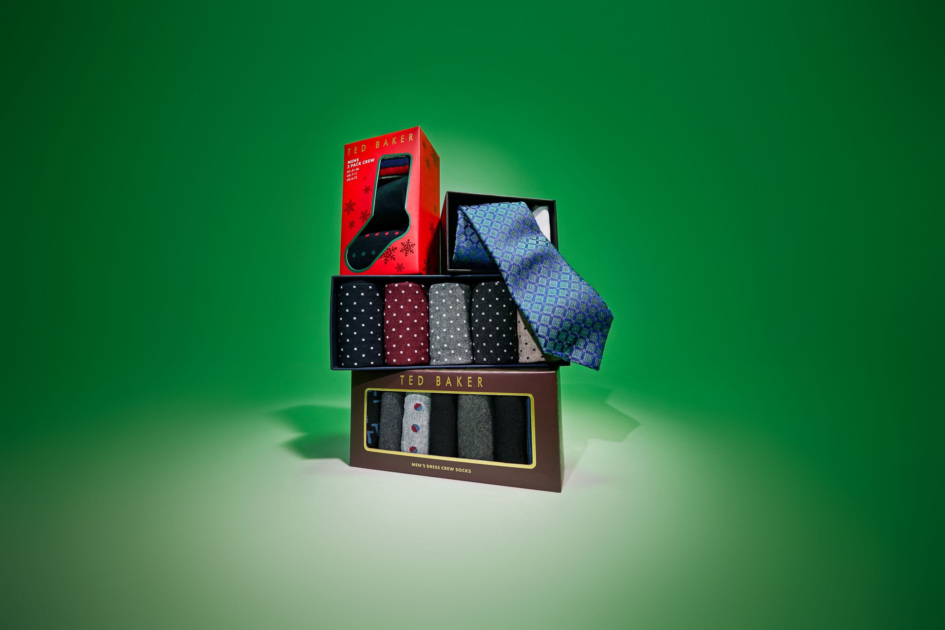 Stacked gift boxes of men's socks and a blue patterned tie on green.