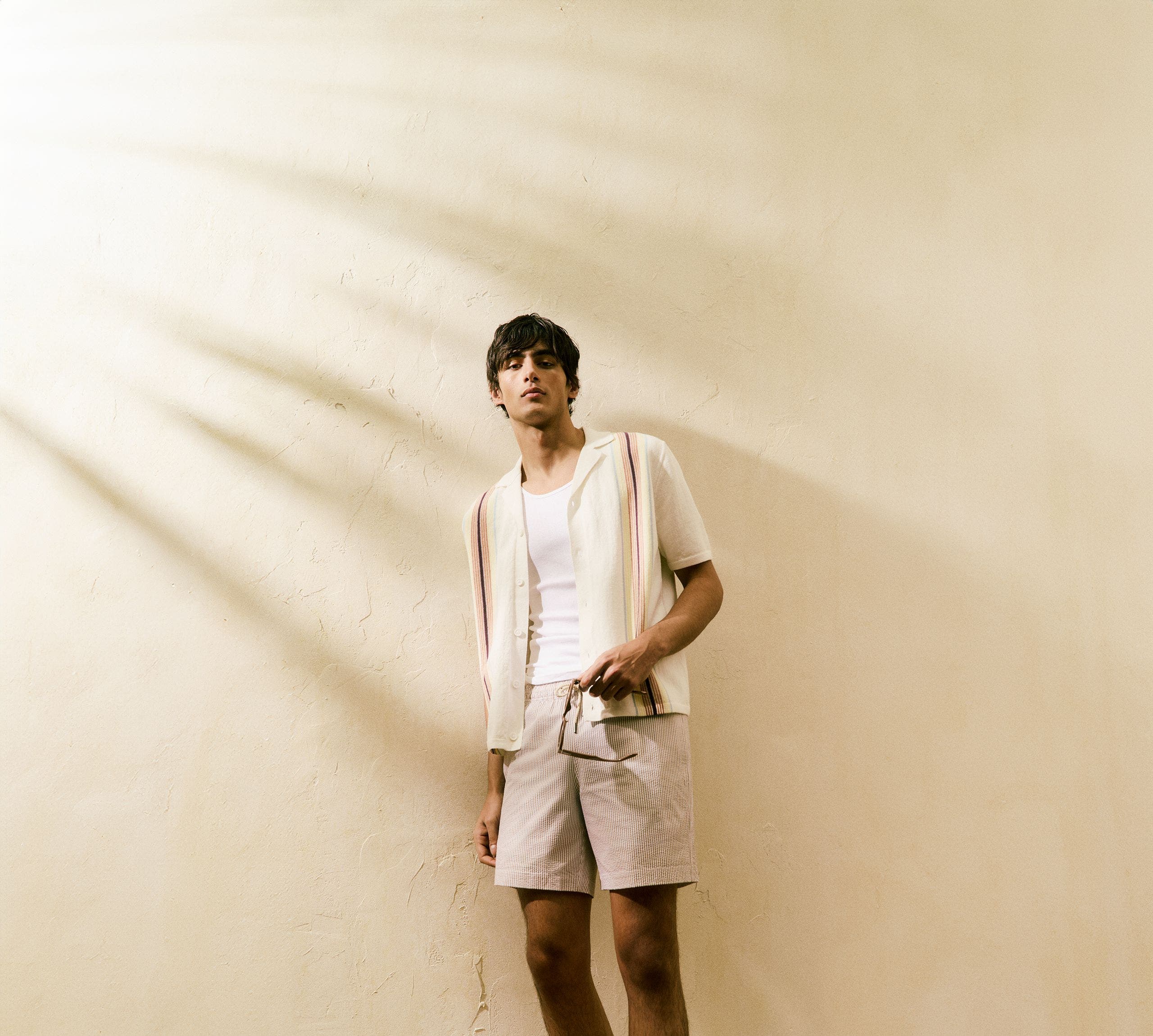 A man wearing a button-up shirt, tee and shorts.