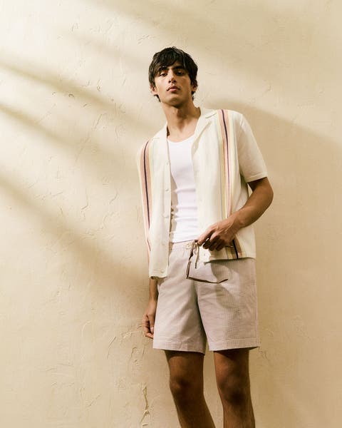 A man wearing a button-up shirt, tee and shorts.